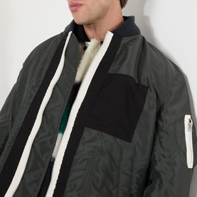 Model wearing SACAI Reversible Bomber Jacket in black, showing contrast white zip, black patch pocket, and layered collar detail.