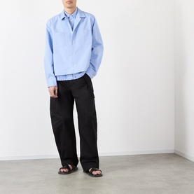 Model wearing Sacai light blue stripe cotton casual shirt with black wide-leg trousers and dark sandals.