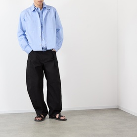 Model wearing Sacai light blue stripe cotton casual shirt with black wide-leg trousers and brown leather sandals