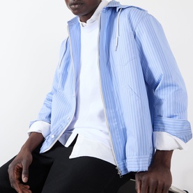 Model wearing SACAI light blue stripe cotton hoodie, open over white top, with black trousers visible