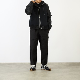 Model wearing Sacai black hoodie with padded nylon overlay, styled with black cargo trousers and black and white trainers.