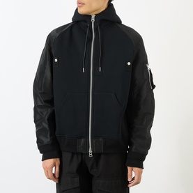 Model wearing Sacai black hoodie with contrast leather-look sleeves, zip front, chest pockets, and hood detail