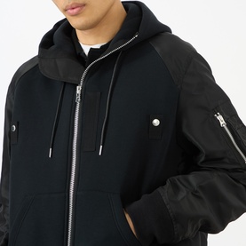Model wearing Sacai Black Hoodie with contrast nylon bomber sleeves, zip front, drawstring hood and silver-tone hardware detail.