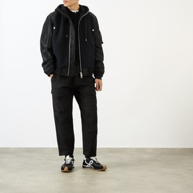 Model wearing Sacai black hoodie with padded nylon sleeves, styled with black tapered trousers and black and white trainers.