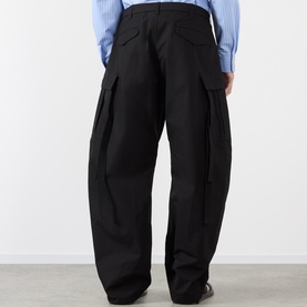 Model wearing Sacai black cotton-nylon cargo trousers with large side pockets, wide leg fit, styled with a light blue shirt.
