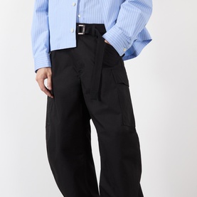 Model wearing Sacai black cotton-nylon casual trousers with cargo pockets and silver belt buckle, styled with a light blue striped shirt.