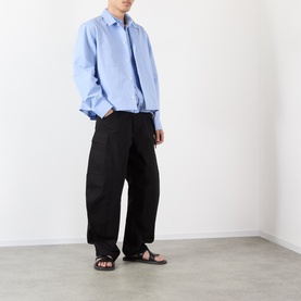 Model wearing Sacai black cotton-nylon casual trousers with wide-leg fit, styled with a light blue shirt and brown sandals.