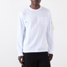 Model wearing Sacai white long-sleeve cotton T-shirt with chest pocket and zip sleeve pocket detail, styled with black trousers.