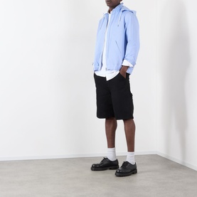 Model wearing Sacai white cotton T-shirt, styled with light blue zip-up hoodie, black shorts, and black loafers