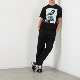 Model wearing Sacai black cotton graphic T-shirt with Muhammad Ali print, styled with black joggers and dark trainers