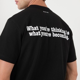 Model wearing Sacai black cotton T-shirt, back view showing white slogan print: "What you're thinking is what you're becoming.
