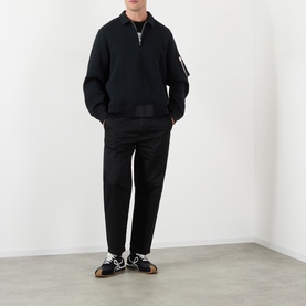 Model wearing SACAI black cotton-blend half-zip polo with matching black trousers and patterned trainers.