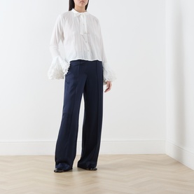 Model wearing Sister Jane white cotton blouse with feather cuffs and button front, styled with wide-leg navy trousers and black shoes.