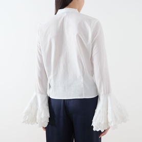 Model wearing Sister Jane white cotton blouse, back view, with fluted ruffle cuffs, paired with navy trousers.