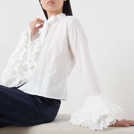 Model wearing Sister Jane white cotton blouse with pintuck front, flared sleeves and lace frill cuffs, styled with navy trousers.