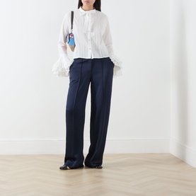 Model wearing Sister Jane white cotton blouse with feather cuffs and pintuck detail, styled with navy wide-leg trousers and black shoes