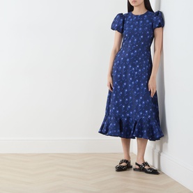 Model wearing Sister Jane navy floral midi dress with puff sleeves and ruffle hem, styled with black strappy flat sandals.