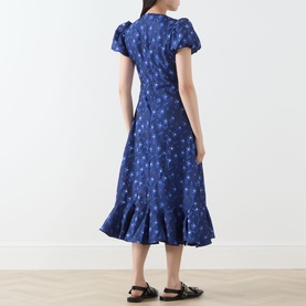 Model wearing Sister Jane navy dress with floral print, puff sleeves, wrap silhouette and ruffle hem, styled with black sandals.