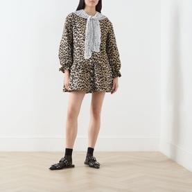 Model wearing Sister Jane multi leopard print mini dress with tie neck collar, styled with black socks and patent loafers