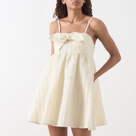 Model wearing Sister Jane Honey Jacquard Mini Dress in cream, featuring bow-embellished square neckline, spaghetti straps and flared skirt