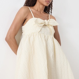 Model wearing Sister Jane Honey Jacquard Mini Dress in cream, featuring bow embellishment at bust and adjustable spaghetti straps