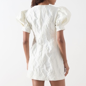 Model wearing Sister Jane Milos Brooches Mini Dress in white jacquard, short puff sleeves, back zip, mini length. Rear view.