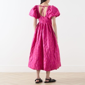 Model wearing Sister Jane pink dress with puff sleeves, open back tie detail, and full midi skirt in textured fabric