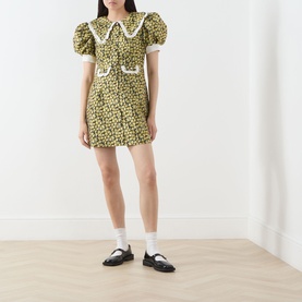 Model wearing Sister Jane olive floral mini dress with lace collar, puff sleeves and bow trim, styled with white socks and black loafers