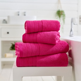 The Lyndon Company Plain Fuschia towel set stacked on a white stool in a bright bathroom setting, showing multiple sizes