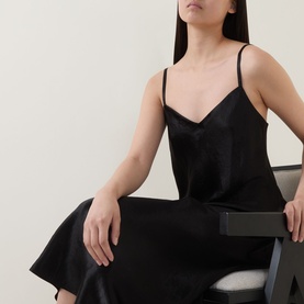 Model wearing Vince Satin Slip Dress in black with V-neckline, slim straps and midi length in smooth satin finish, seated on chair.