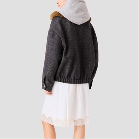 Model wearing Maje dark grey hooded jacket with faux fur trim collar, styled with white lace-hem dress, back view