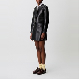 Model wearing Claude Pierlot black faux leather mini skirt and matching jacket, styled with white collar top, yellow socks and brown loafers