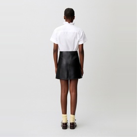 Model wearing Claude Pierlot black mini skirt, rear view, styled with white short-sleeve shirt, yellow socks and black loafers