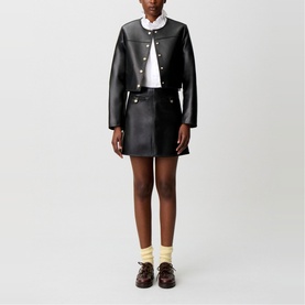 Model wearing Claude Pierlot black faux leather cropped jacket and mini skirt, styled with white shirt, cream socks and dark loafers
