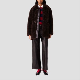 Model wearing Maje dark brown textured faux shearling coat with black leather wide-leg trousers and red loafers