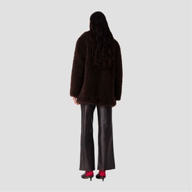 Model wearing Maje dark brown shaggy faux fur coat, styled with black flared leather trousers and red heels, rear view