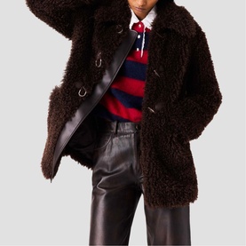 Model wearing Maje dark brown shearling coat with gold-tone fastenings, styled with striped rugby top and dark leather trousers