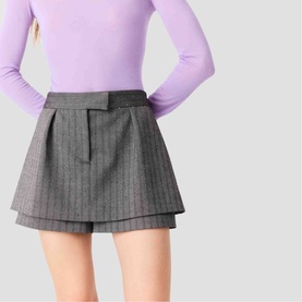 Model wearing Maje grey pinstripe layered mini skirt with pleated detail, styled with a lilac long-sleeve top