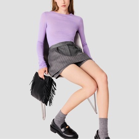 Model wearing Maje Womens French Dress in lavender long-sleeve top and grey pinstripe mini skirt, carrying black fringed clutch bag