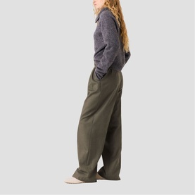 Model wearing Maje red wide-leg trousers with a grey knit top and cream shoes, side profile view.