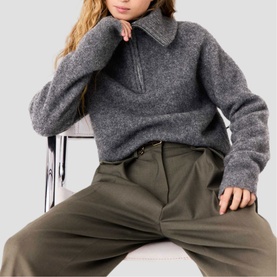 Model wearing Maje red half-zip knit sweater, styled with khaki wide-leg trousers, seated pose
