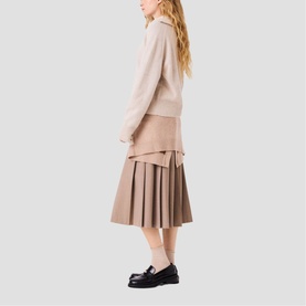 Model wearing Maje clear tonal knit top and pleated midi skirt, styled with black loafers, shot from behind