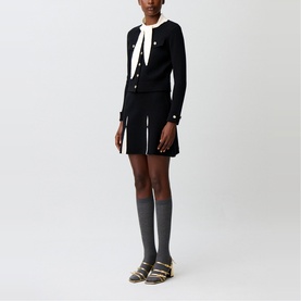 Model wearing Claude Pierlot black knit cardigan with gold buttons and white trim, styled with matching mini skirt, grey knee socks and brown sandals.