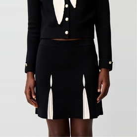 Model wearing Claude Pierlot black mini skirt with cream pleat inserts, styled with matching black cropped cardigan with gold buttons.