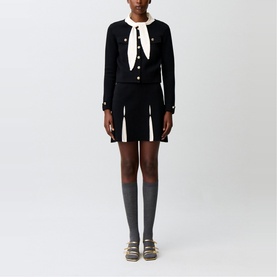 Model wearing Claude Pierlot black knit cardigan and mini skirt set with cream collar detail, styled with grey knee socks and flat sandals.