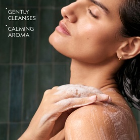 Model applying Aveda Shampure Calming Body Wash to shoulder, lathering in a steam-filled shower
