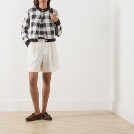 Model wearing Barbour International multi check cardigan in black and white, styled with cream tailored shorts and brown loafers.