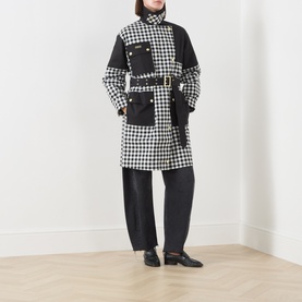 Model wearing Barbour International Gea Gingham Showerproof Coat in black, longline with patch pockets and belt, styled with black wide-leg trousers