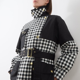 Model wearing Barbour International Gea Gingham Showerproof Coat in black, featuring contrast gingham panels, gold press-studs, and adjustable belt