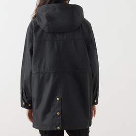 Model wearing Barbour International Molina Showerproof Coat in black, rear view showing detachable hood, studded back vent and gold snap button cuffs.